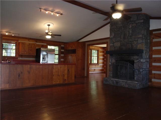 unfurnished living room with ceiling fan, wood-type flooring, healthy amount of natural light, wood walls, and vaulted ceiling