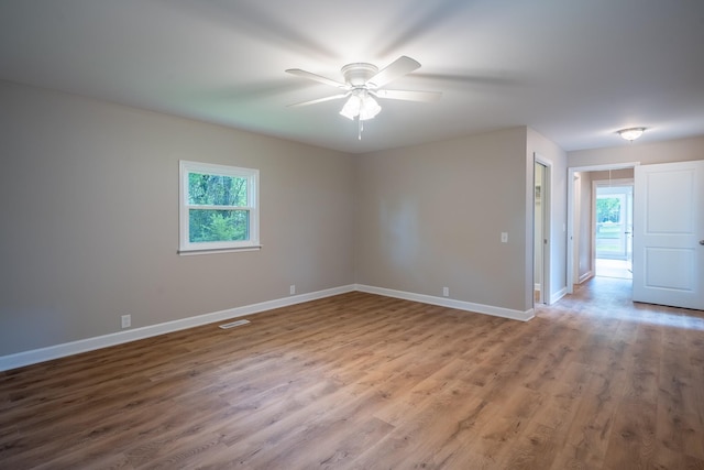 unfurnished room featuring healthy amount of natural light, wood finished floors, a ceiling fan, and baseboards