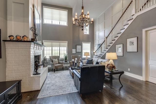 living area featuring a chandelier, dark wood-style flooring, a towering ceiling, a fireplace, and baseboards
