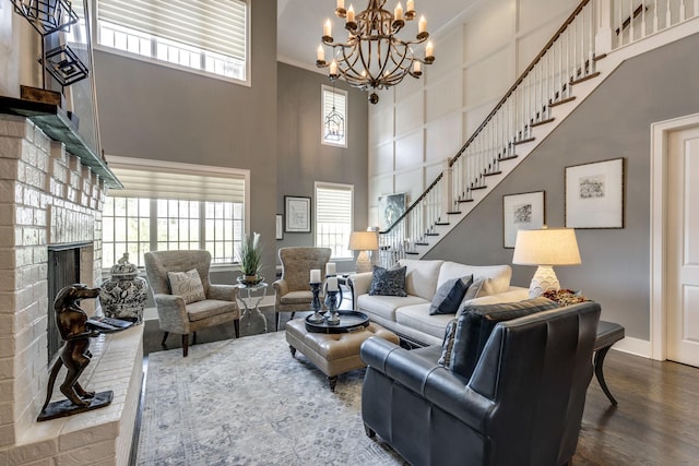 living area featuring a high ceiling, wood finished floors, plenty of natural light, stairs, and a brick fireplace