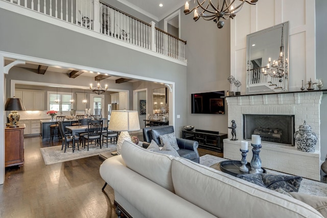 living room featuring a chandelier, a brick fireplace, dark wood finished floors, a high ceiling, and beam ceiling