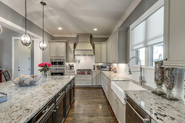 kitchen featuring custom exhaust hood, a sink, appliances with stainless steel finishes, tasteful backsplash, and light stone counters