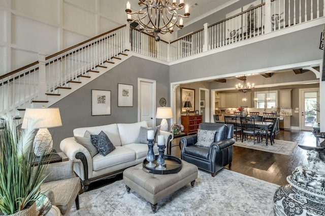 living room with a towering ceiling, a chandelier, stairs, and dark wood-type flooring