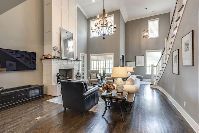 living area featuring dark wood-style flooring, a chandelier, a towering ceiling, plenty of natural light, and a fireplace