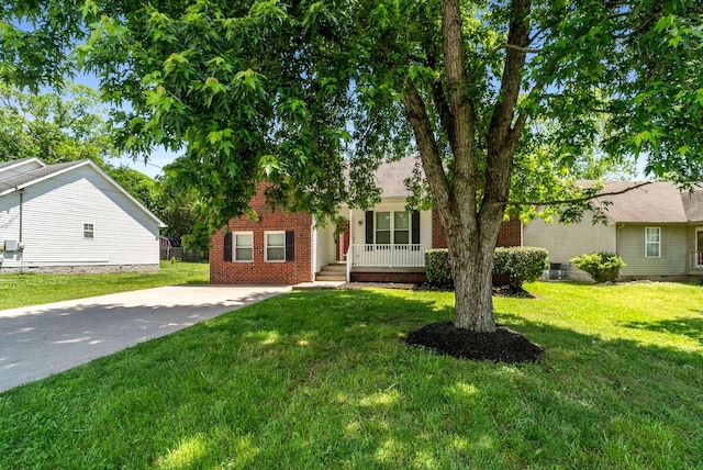 view of property hidden behind natural elements with a porch, a front yard, brick siding, and concrete driveway