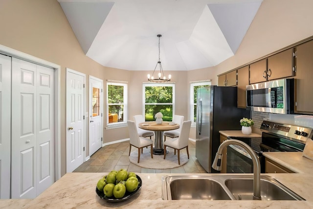 kitchen featuring stainless steel appliances, a sink, vaulted ceiling, a chandelier, and light countertops