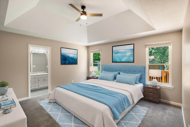 bedroom featuring a raised ceiling, carpet floors, connected bathroom, baseboards, and a ceiling fan