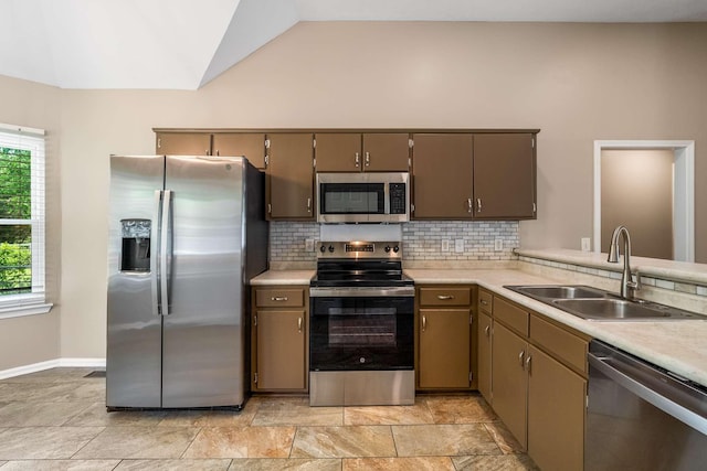 kitchen featuring stainless steel appliances, a sink, tasteful backsplash, vaulted ceiling, and light countertops