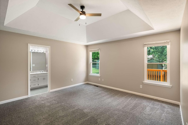 unfurnished bedroom featuring carpet floors, a tray ceiling, multiple windows, and connected bathroom