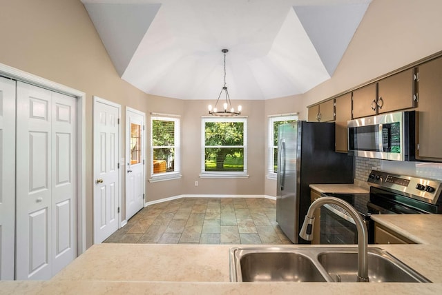 kitchen featuring appliances with stainless steel finishes, a sink, a chandelier, baseboards, and stone tile flooring