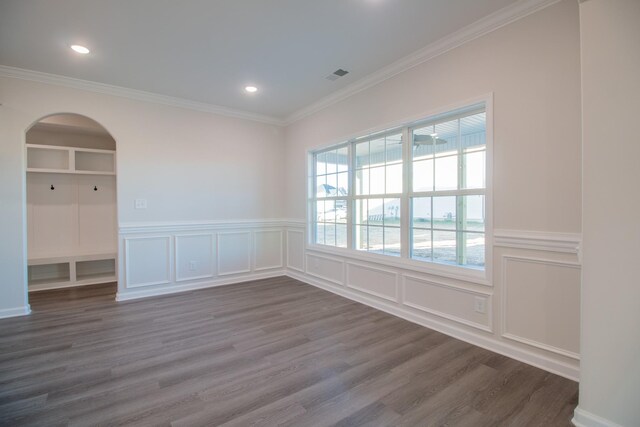 empty room featuring crown molding, dark wood-style flooring, arched walkways, wainscoting, and a decorative wall