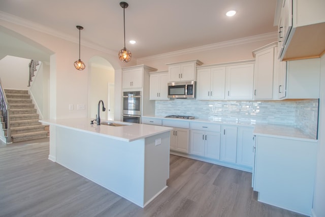 kitchen featuring appliances with stainless steel finishes, a sink, light wood finished floors, arched walkways, and light countertops