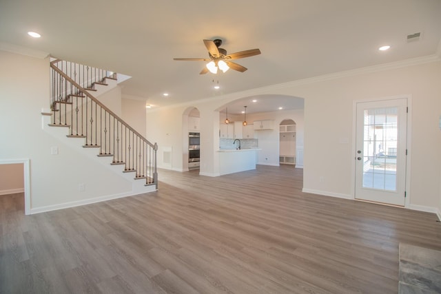 unfurnished living room with arched walkways, a ceiling fan, ornamental molding, wood finished floors, and recessed lighting