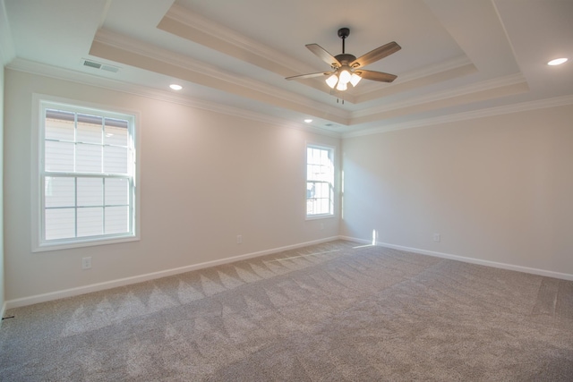 empty room with a tray ceiling, ornamental molding, ceiling fan, carpet floors, and baseboards