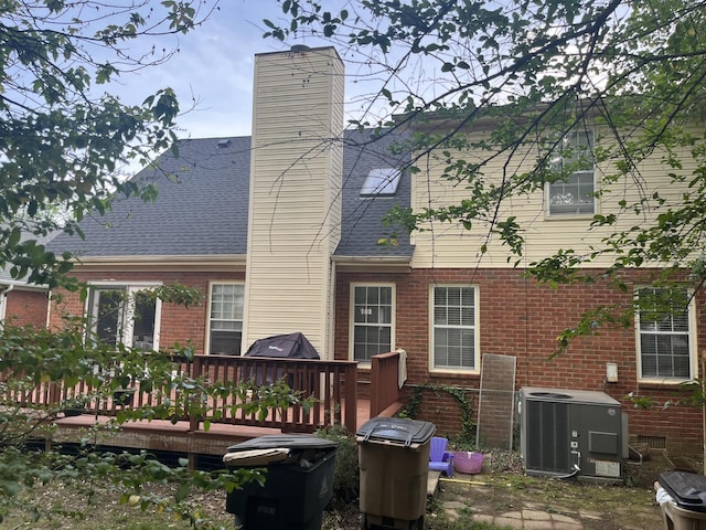 back of house with central AC, brick siding, a wooden deck, and a chimney