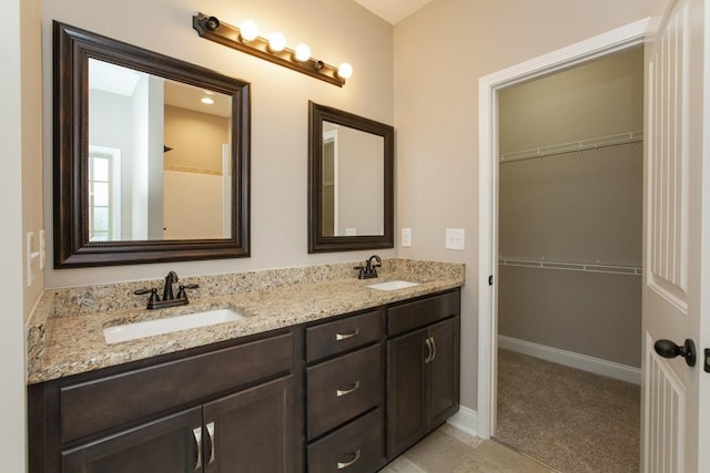 full bathroom with a walk in closet, double vanity, and baseboards