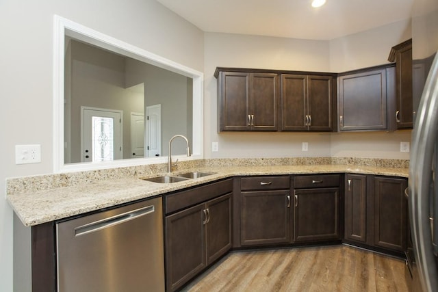 kitchen featuring appliances with stainless steel finishes, a sink, dark brown cabinetry, light wood-style flooring, and light stone countertops