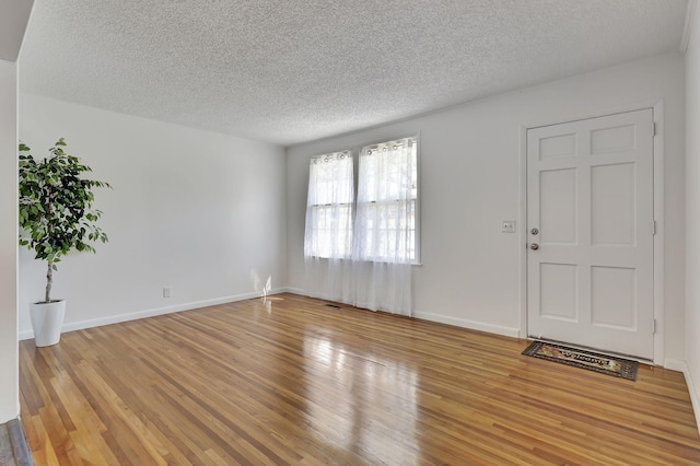 unfurnished living room featuring a textured ceiling, wood finished floors, and baseboards
