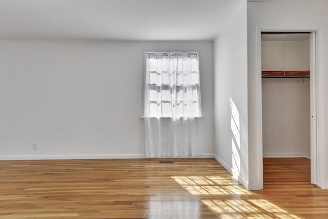 unfurnished bedroom with light wood-type flooring, a closet, a walk in closet, and baseboards