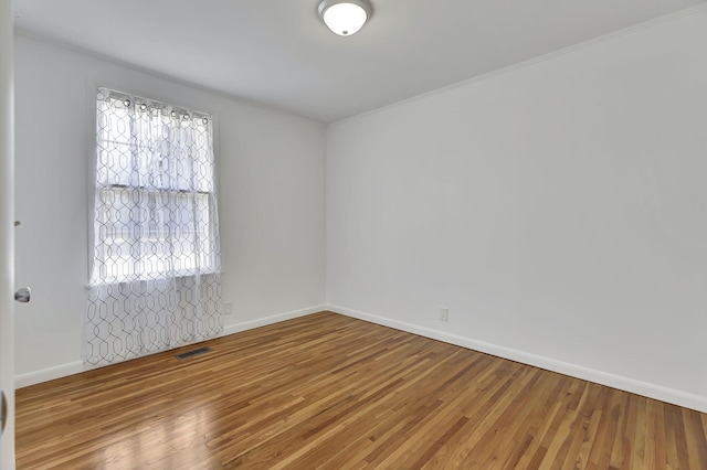 spare room with baseboards, wood finished floors, and crown molding