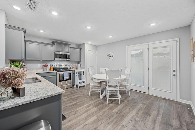 kitchen featuring appliances with stainless steel finishes, gray cabinets, light wood-style flooring, light stone counters, and recessed lighting