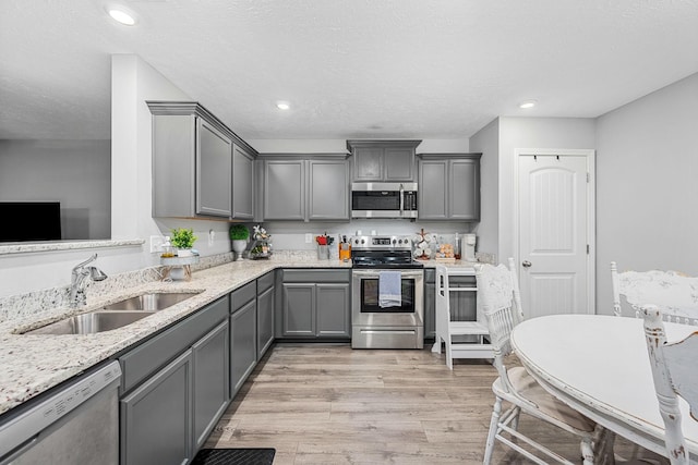 kitchen featuring stainless steel appliances, gray cabinets, light wood-type flooring, a sink, and light stone countertops