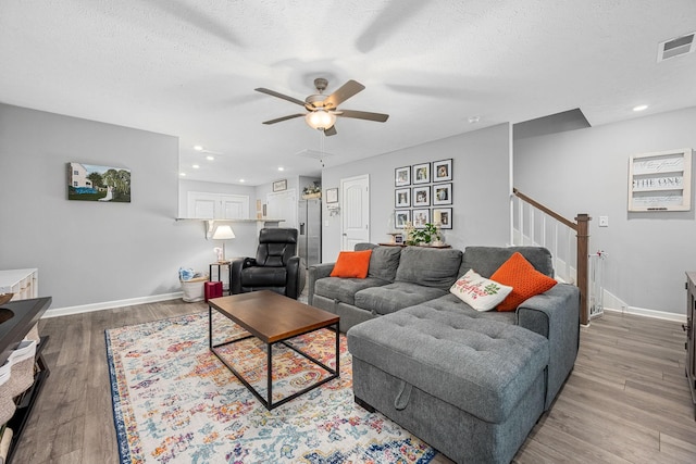 living room featuring ceiling fan, stairway, light wood-style flooring, baseboards, and recessed lighting