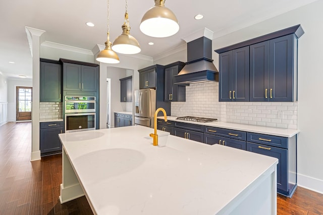 kitchen featuring custom range hood, appliances with stainless steel finishes, a kitchen island with sink, light countertops, and ornamental molding
