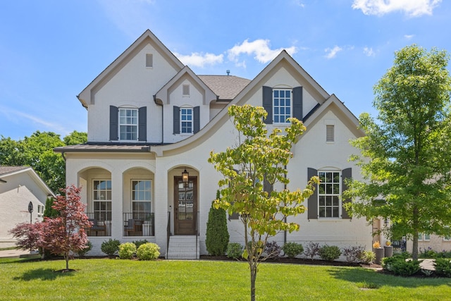 view of front facade with covered porch, a standing seam roof, a front lawn, and stucco siding