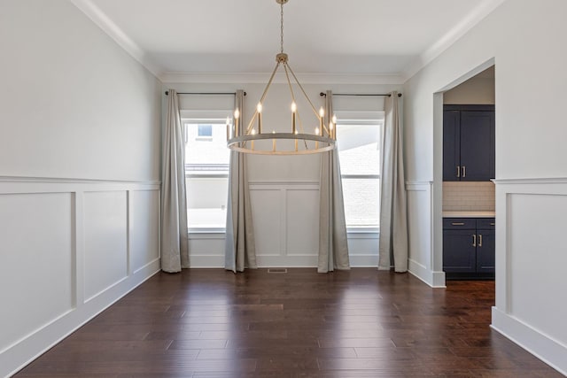 unfurnished dining area with a chandelier, a decorative wall, wainscoting, dark wood finished floors, and ornamental molding