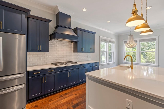 kitchen with stainless steel appliances, custom range hood, a sink, blue cabinets, and light countertops