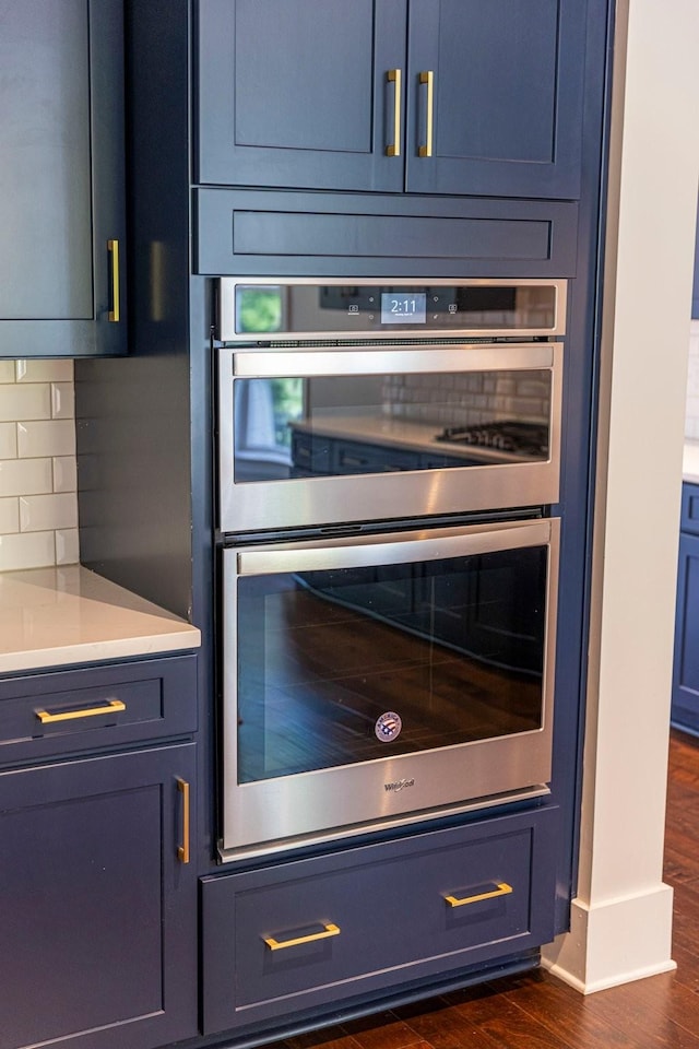 kitchen view of double oven, backsplash, dark wood finished floors, and light countertops