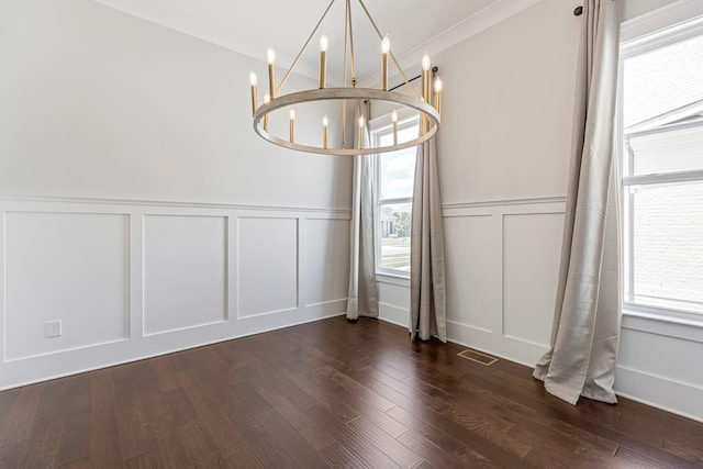 unfurnished dining area featuring a decorative wall, healthy amount of natural light, a chandelier, wainscoting, and dark wood-style floors