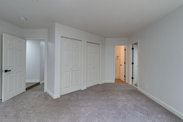 unfurnished bedroom featuring two closets, carpet flooring, and baseboards