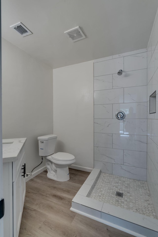 bathroom featuring toilet, tiled shower, wood finished floors, vanity, and baseboards
