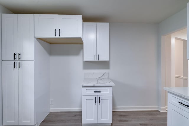 kitchen featuring dark wood-type flooring, light stone counters, white cabinetry, and baseboards