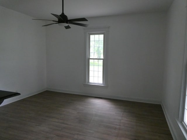 empty room with plenty of natural light, dark wood-type flooring, a ceiling fan, and baseboards