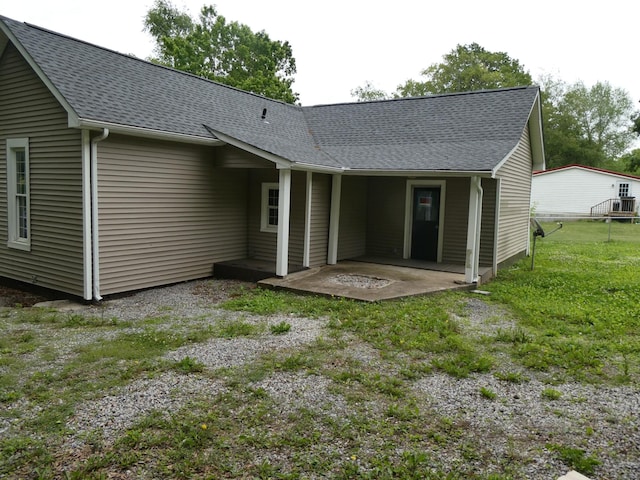 rear view of property featuring a patio area, a shingled roof, and a lawn