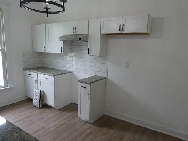 kitchen with under cabinet range hood, light wood-type flooring, backsplash, and white cabinetry