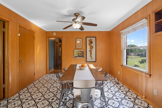 dining room featuring a ceiling fan, ornamental molding, wood walls, and baseboards