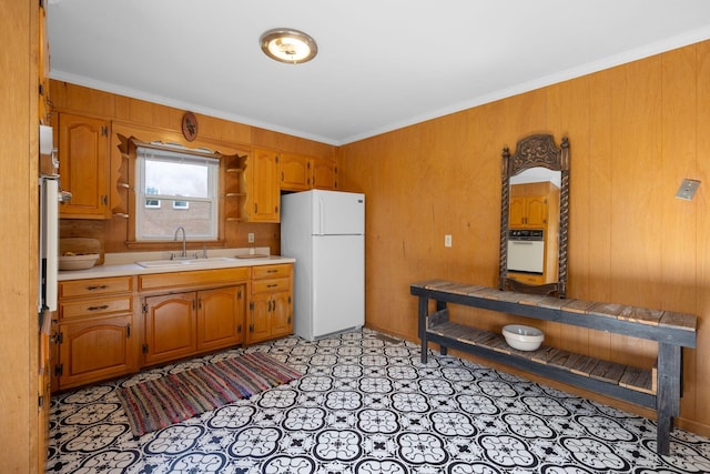 kitchen featuring white appliances, ornamental molding, a sink, light countertops, and brown cabinetry