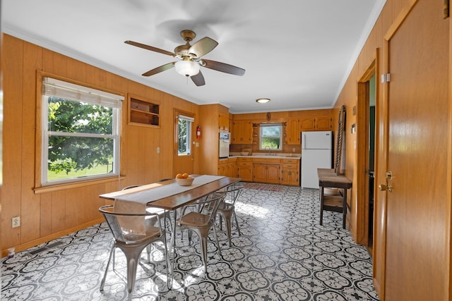 dining area featuring wood walls, ceiling fan, and crown molding