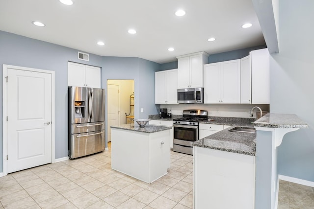 kitchen with stainless steel appliances, a sink, a peninsula, dark stone countertops, and recessed lighting