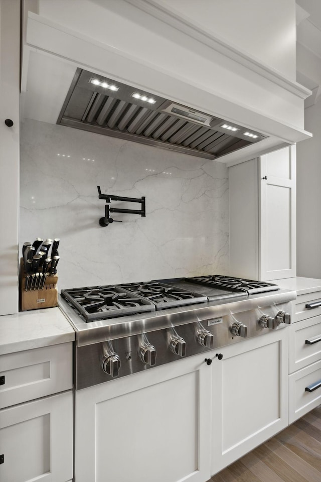 kitchen featuring stainless steel gas cooktop, tasteful backsplash, white cabinets, premium range hood, and wood finished floors
