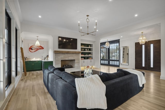 living room featuring a chandelier, a fireplace, light wood-style flooring, built in shelves, and crown molding