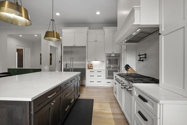 kitchen with custom range hood, white cabinets, stainless steel appliances, a center island, and decorative light fixtures