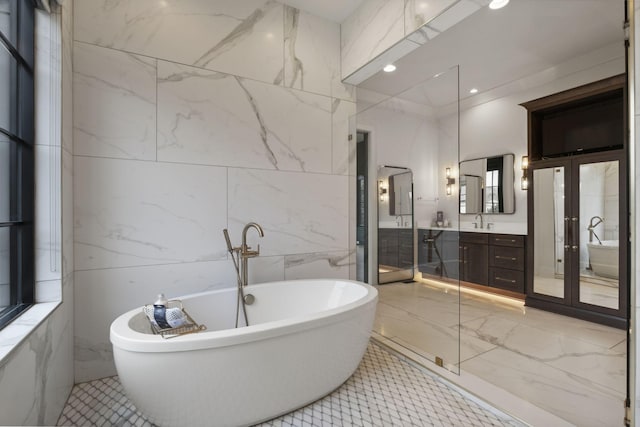 bathroom with a freestanding tub, vanity, tile walls, and marble finish floors
