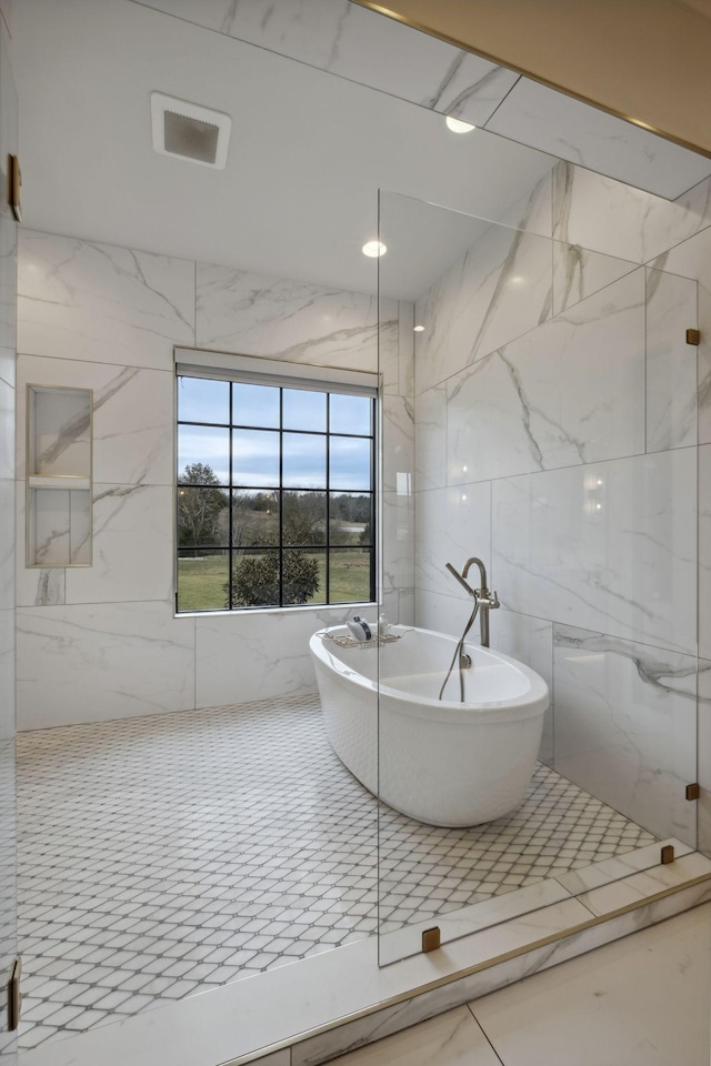 full bathroom with tile walls, a freestanding bath, and a marble finish shower