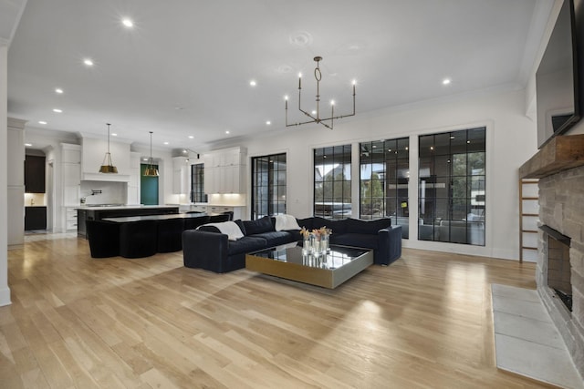 living room with a stone fireplace, ornamental molding, recessed lighting, light wood-style floors, and a chandelier