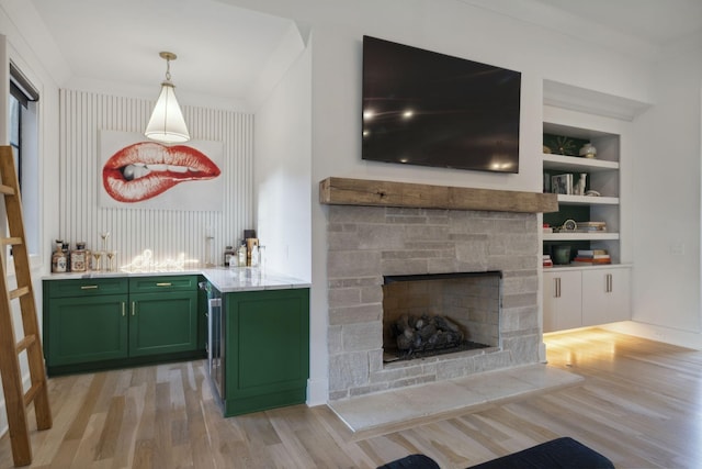 bar area with light wood-style floors, a stone fireplace, built in features, and pendant lighting
